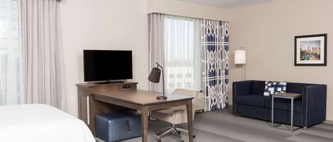 A hotel room with a bed, a desk with a TV, a sofa, and a lamp.