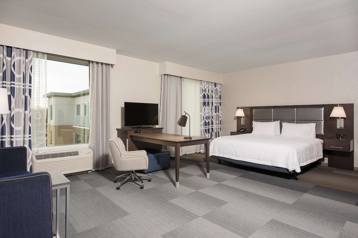 A hotel room with a bed, desk, chair, TV, and a window with curtains.