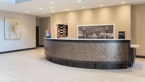 A modern hotel reception area with a curved reception desk, a framed cityscape artwork, and a digital screen displaying the word "explore". - Hampton  Inn & Suites Indianapolis-Keystone (Indianapolis)