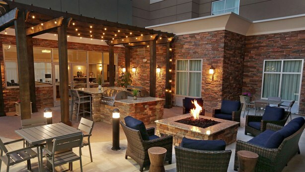 Un patio al aire libre con un hogar para fuego, mobiliario de mimbre y una pérgola con luces colgantes.