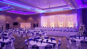 Un salón de banquetes con mesas redondas, manteles blancos y cintas azules.