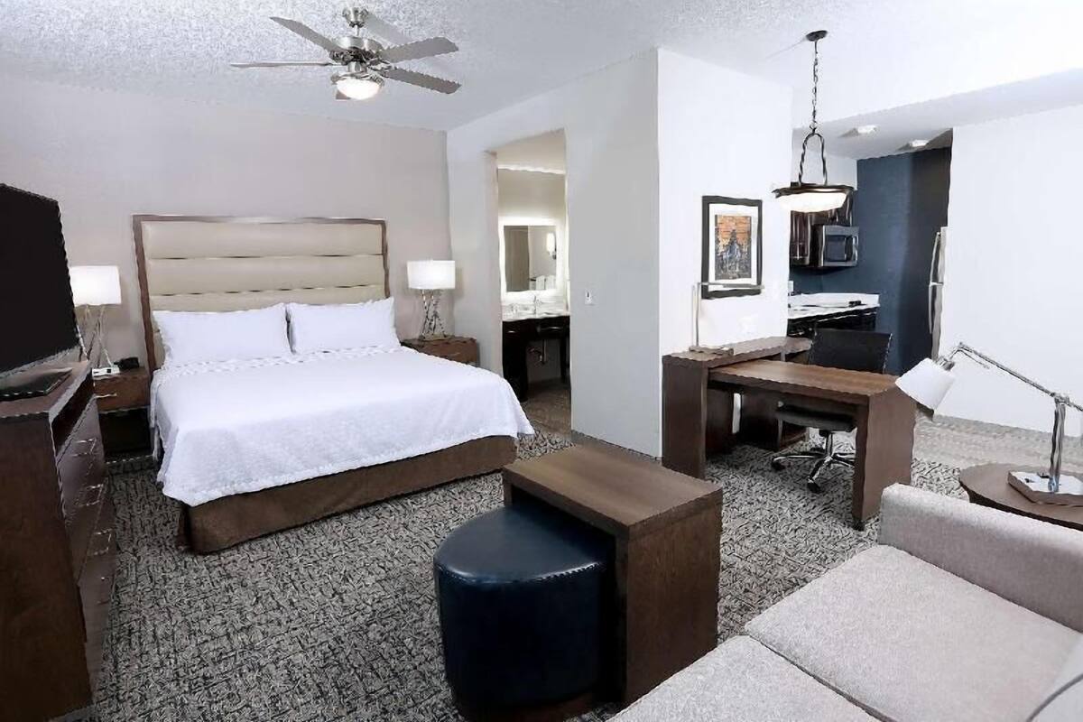 A hotel room with a bed, a desk, a chair, a sofa, a ceiling fan, and a television.