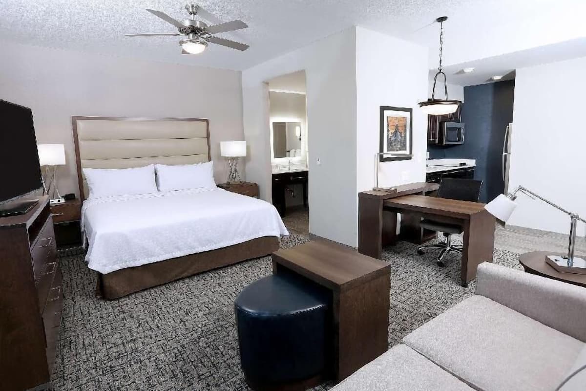 A hotel room with a bed, a desk, a chair, a sofa, a ceiling fan, and a television.