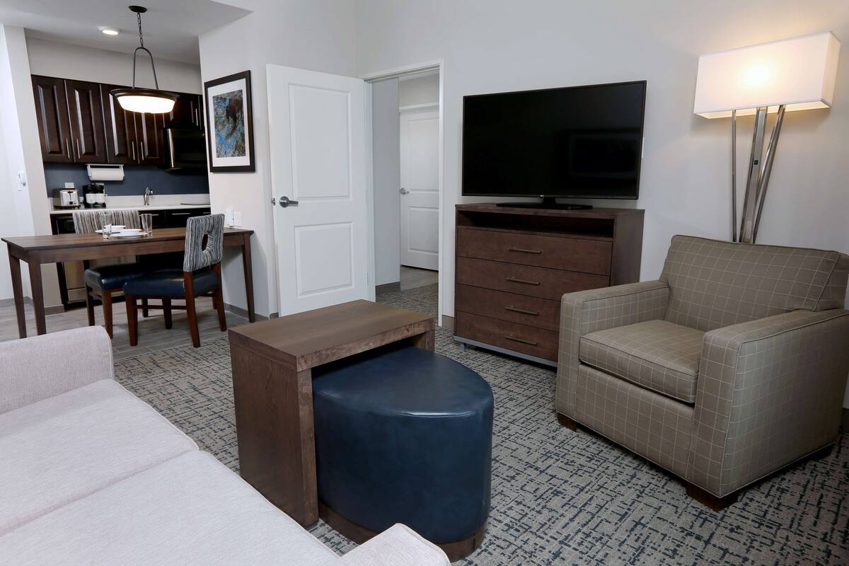 A living room with a sofa, ottoman, TV, and a dining area with chairs and a table.