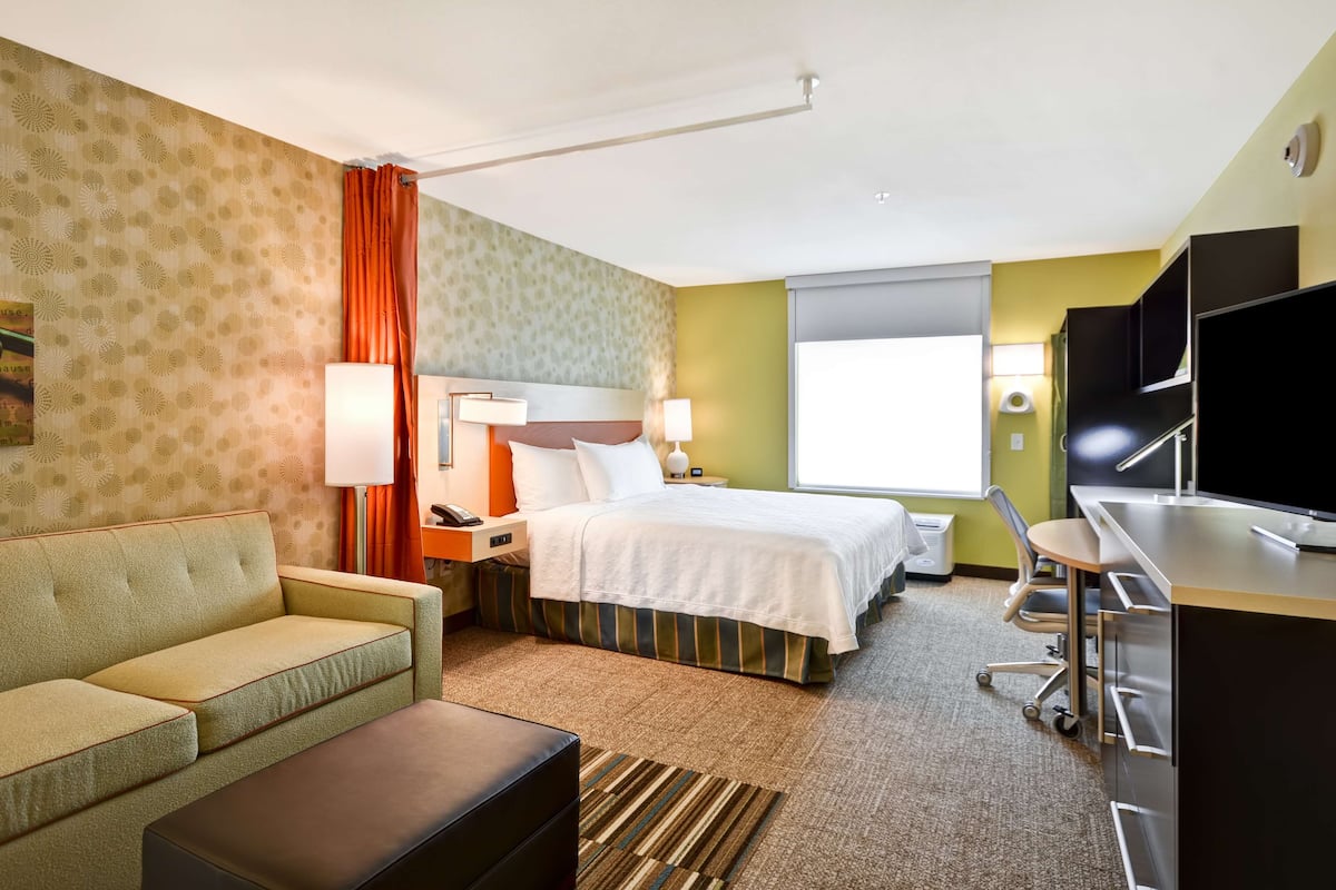 A hotel room with a bed, a sofa, a desk, and a television.