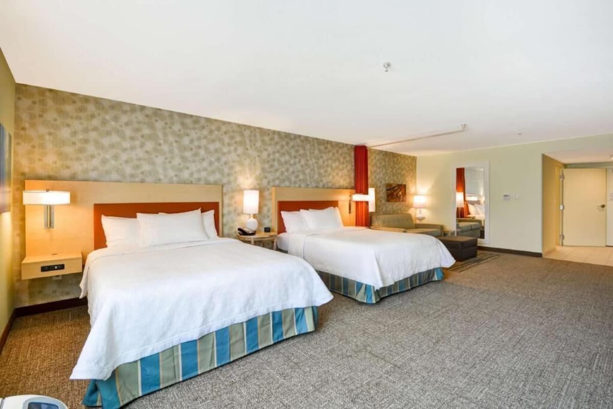 A hotel room with two beds, a carpeted floor, and a small seating area.