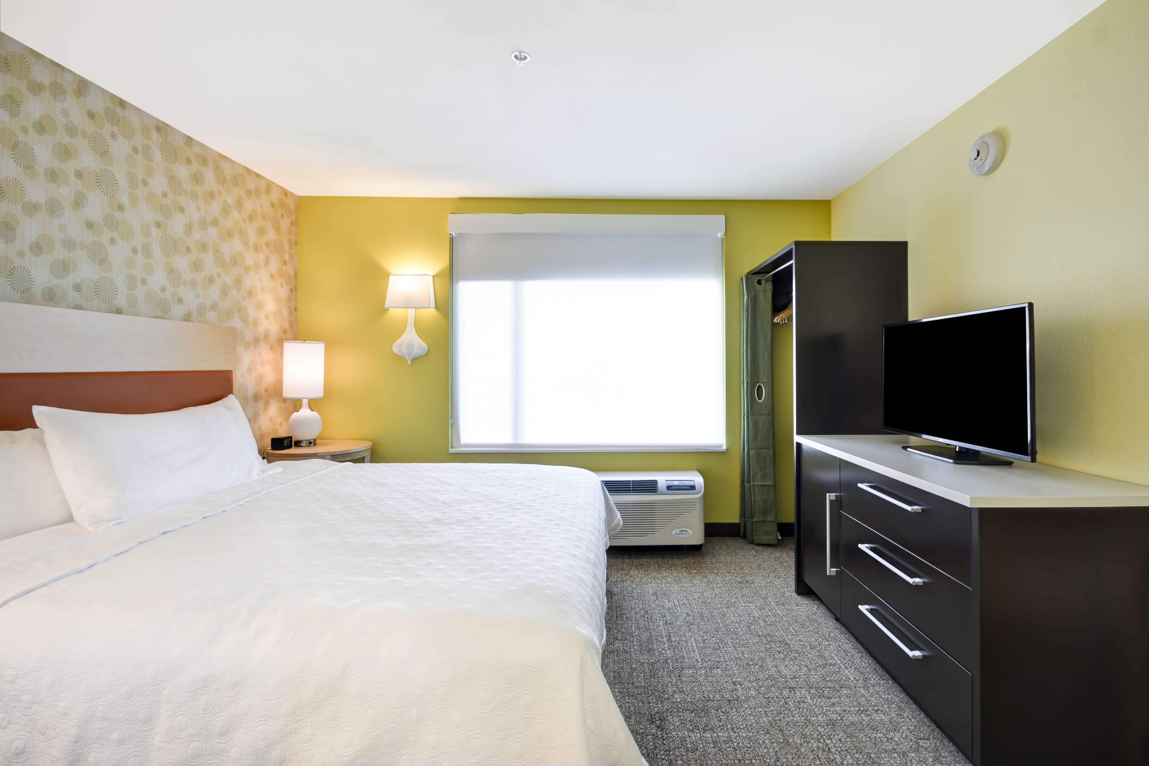 A hotel room with a bed, a television, a desk, and a window.