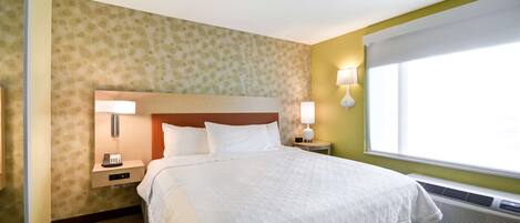 A hotel room with a large bed, two bedside tables with lamps, a wall-mounted phone, and a window with blinds.