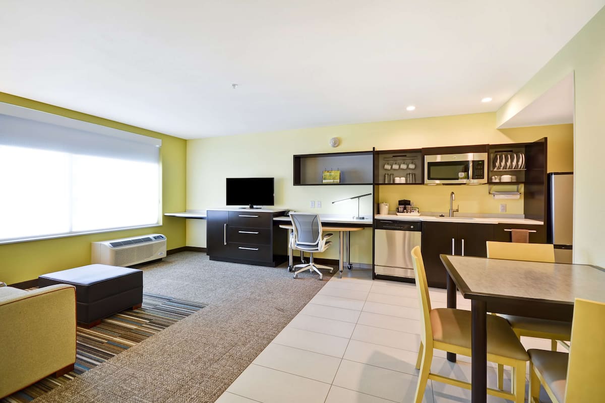 A compact hotel room with a kitchenette, a dining area, and a seating space.