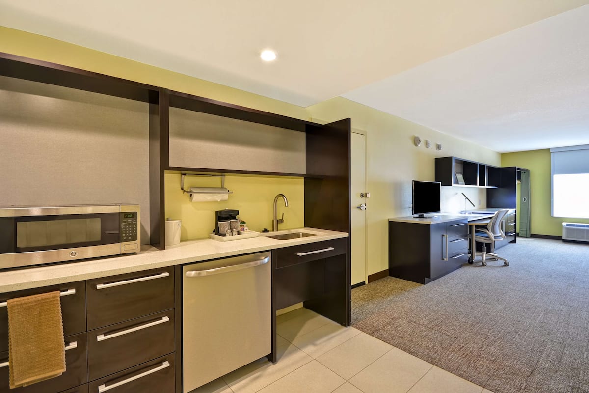 A modern kitchen with a microwave, sink, and dishwasher. There is a small countertop with a coffee maker and a towel hanging on the cabinet.