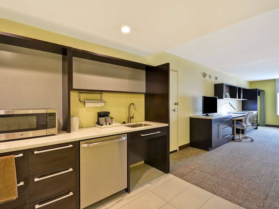 A modern kitchen with a microwave, sink, and dishwasher. There is a small countertop with a coffee maker and a towel hanging on the cabinet.