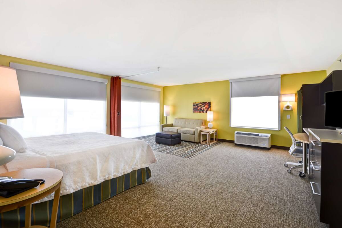 A hotel room with a bed, a desk, a chair, a sofa, and a TV.