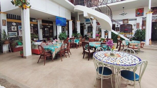 Amplio espacio interior con varias mesas y sillas de comedor, una escalera y diversas plantas en macetas.