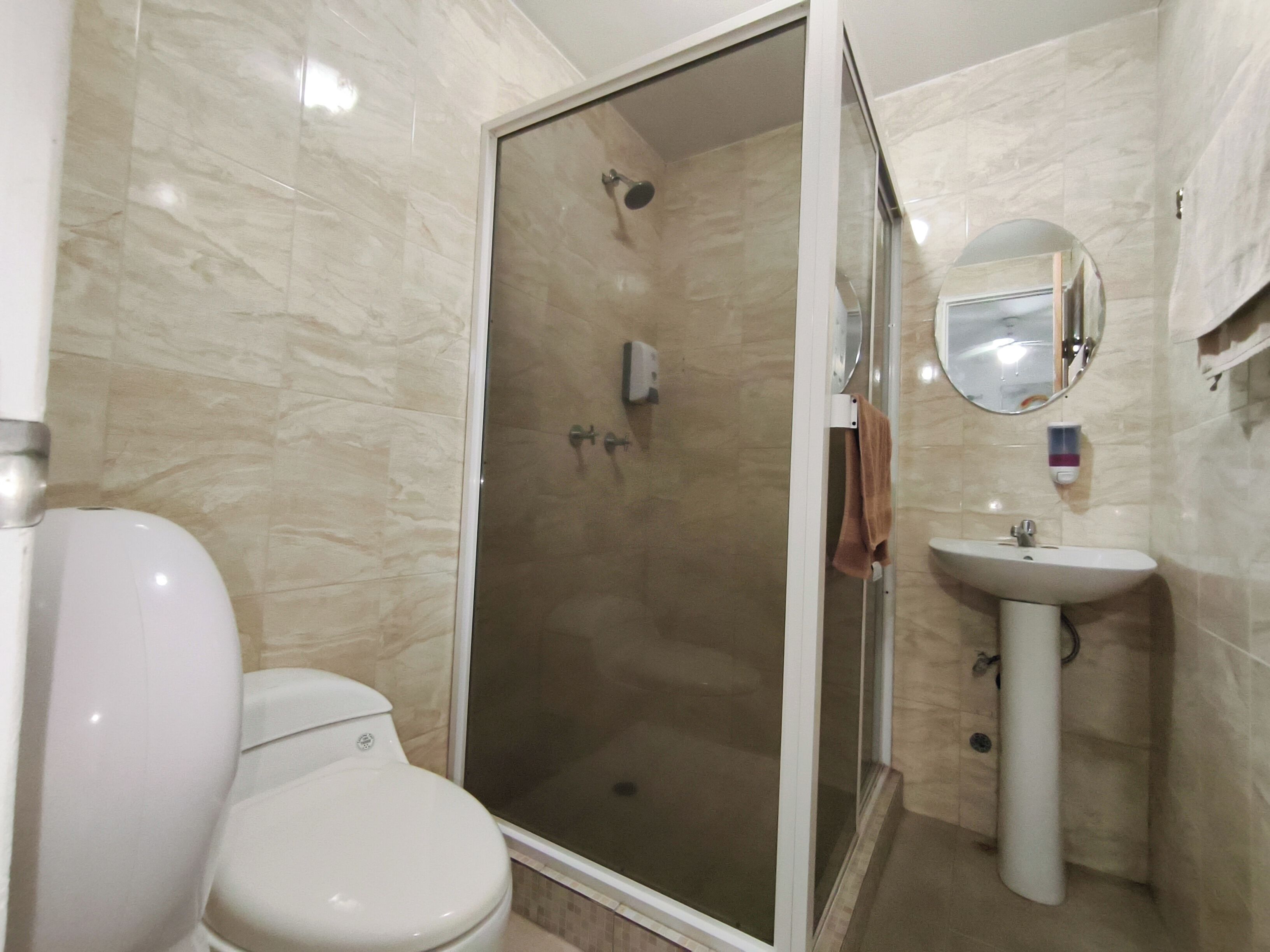 Une salle de bain comprenant des toilettes, une douche fermée par une paroi de verre et un lavabo sur colonne.