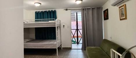Una habitación con literas, un sofá verde, un ventilador de techo y una cama con toallas azules.
