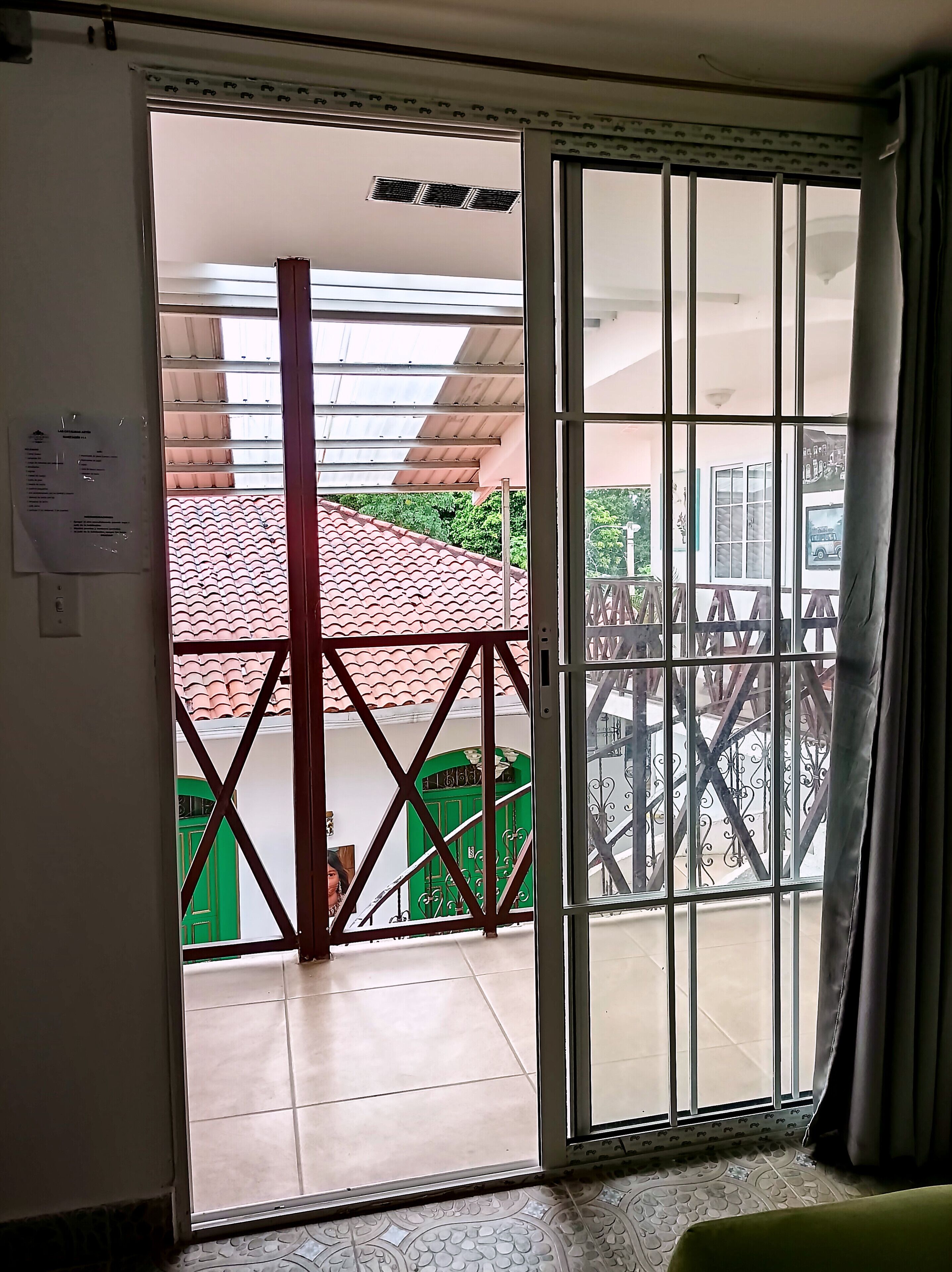 Habitació amb una porta corredissa de vidre que dona a un balcó amb terra de rajola i una porta verda.