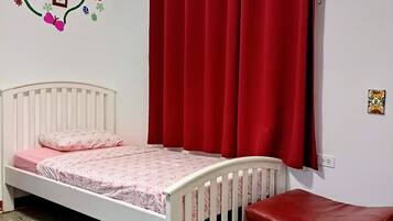 A room with a white bed, red curtains, a red bench, and a wall with a floral decoration.