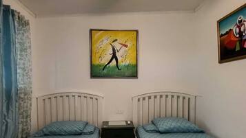 Een kamer met twee eenpersoonsbedden, een plafondventilator, een schilderij aan de muur en een raam met gordijnen.