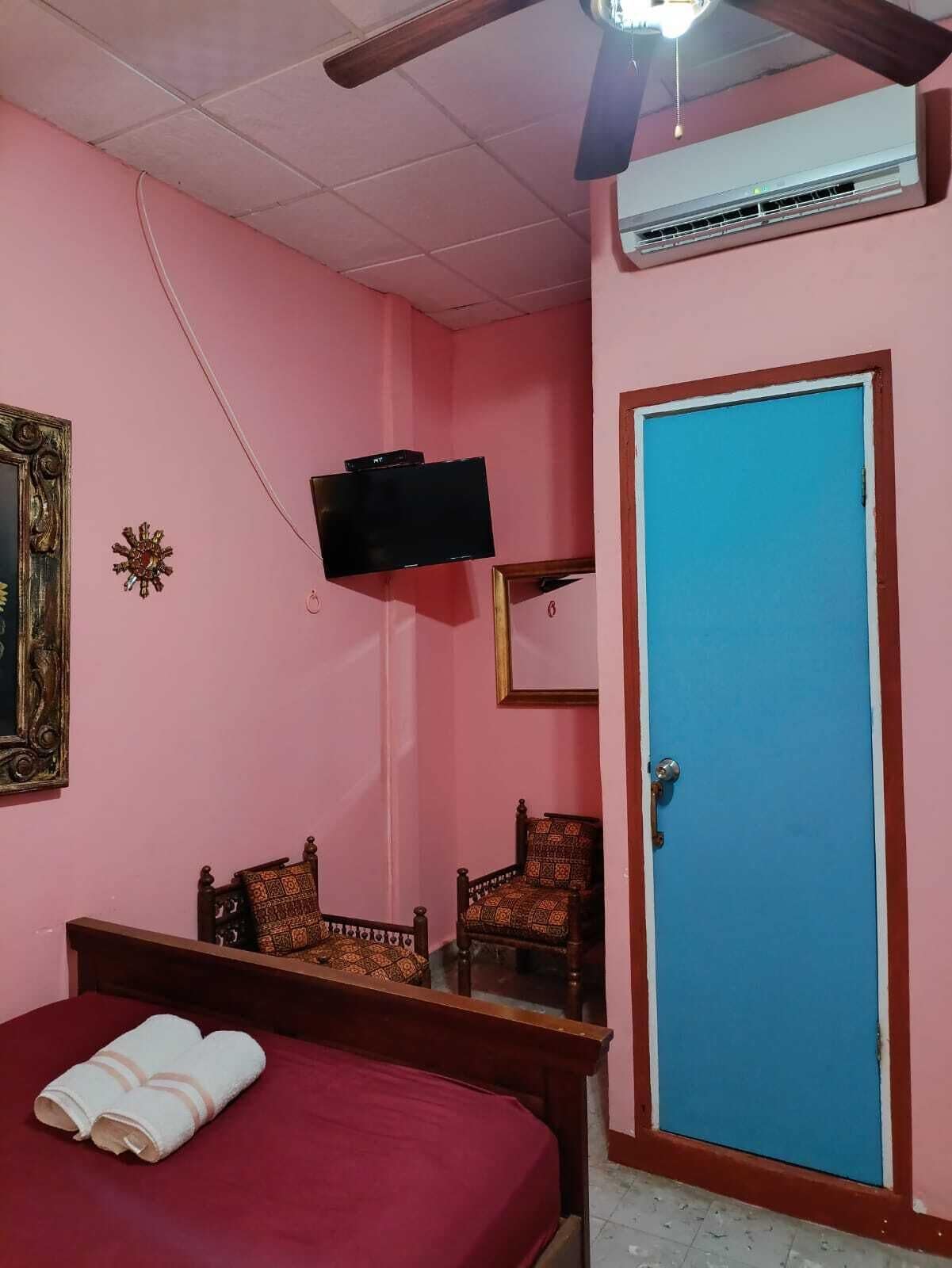 A bedroom with a bed, two chairs, a television, a door, and an air conditioning unit.
