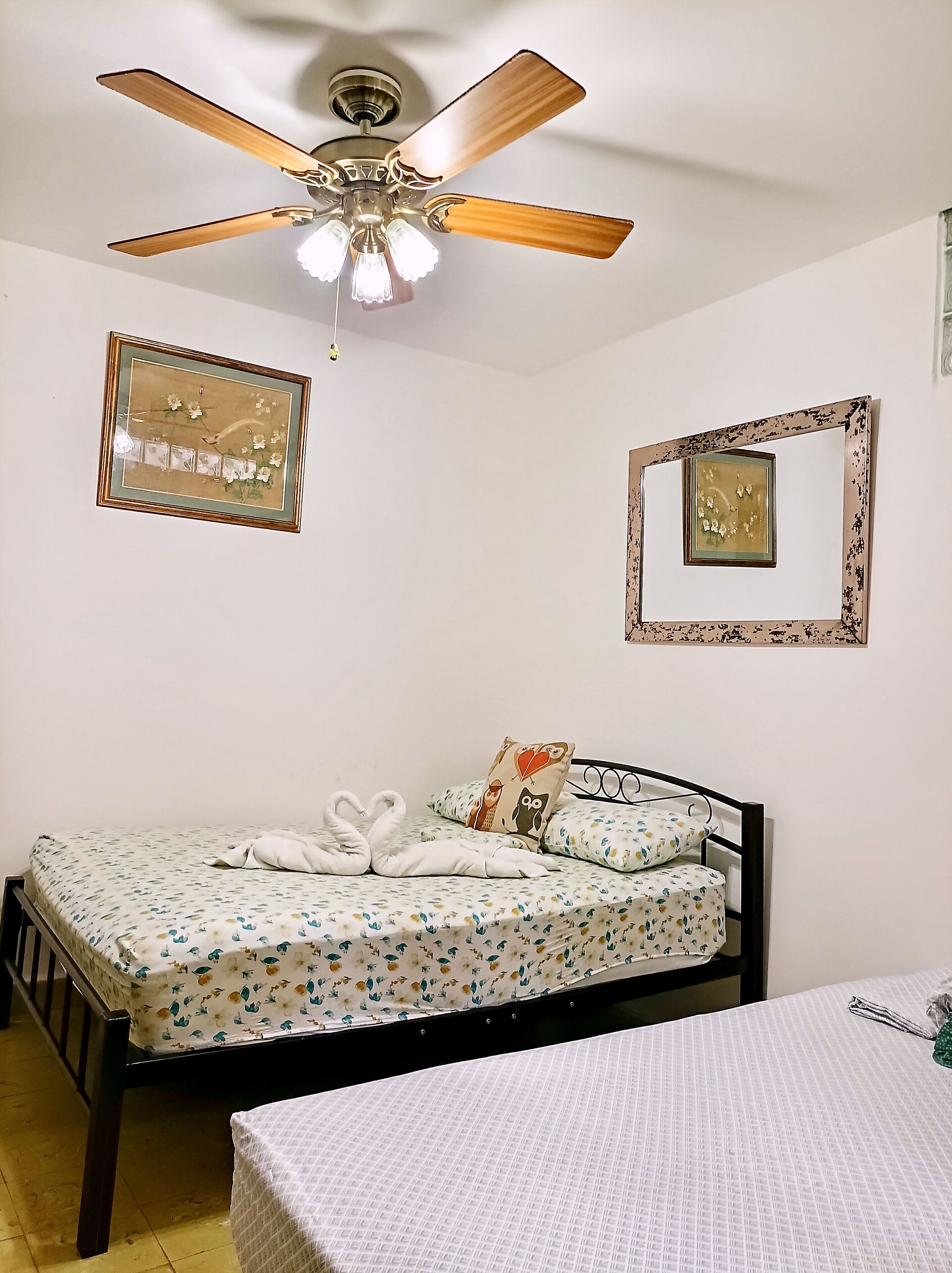 Un dormitorio con una cama, un ventilador de techo y dos cuadros en la pared.