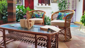 Un patio con sillas de mimbre, una mesa de vidrio y piso de baldosas.