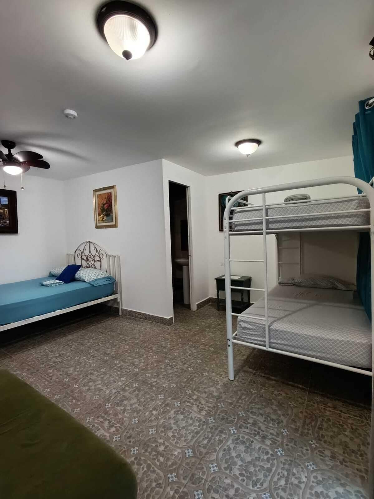 Een kamer met een stapelbed, een eenpersoonsbed, een plafondventilator en een klein tafeltje.