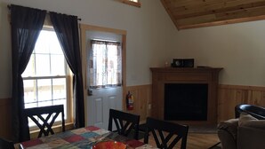 Un coin repas agrémenté d’un plafond en bois, d’une cheminée et d’une table recouverte d’une courtepointe aux couleurs vives.