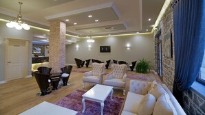 A modern lounge area with a brick column, seating, a TV, and a stone wall. - Casa Gaçe Hotel (Qendër Bulgarec)