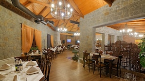 A restaurant with wooden beams, stone walls, and multiple dining tables set with white tablecloths and chairs. - Casa Gaçe Hotel (Qendër Bulgarec)