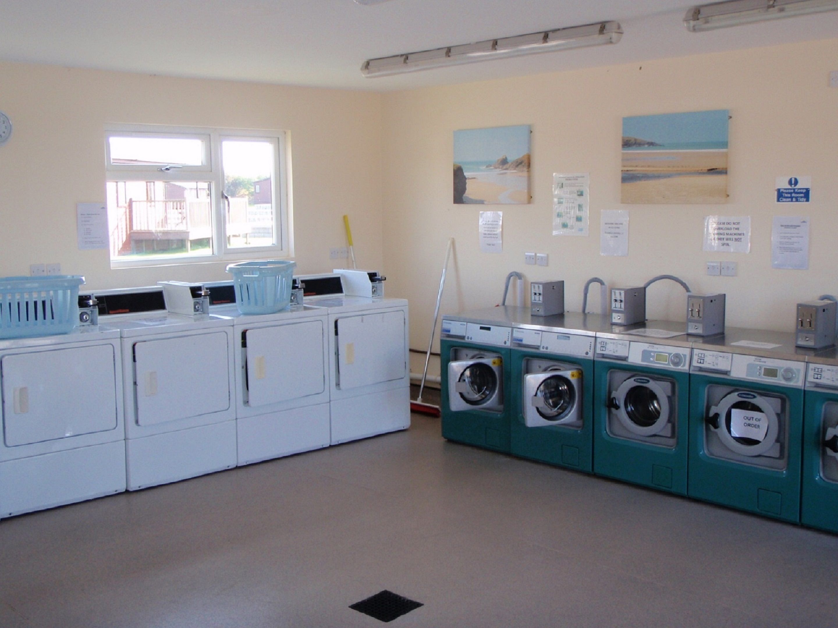 A laundry room with multiple washing machines and dryers, a window, and a view of the beach.