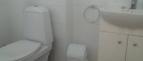 A bathroom with a toilet, a trash bin, and a sink with a mirror.