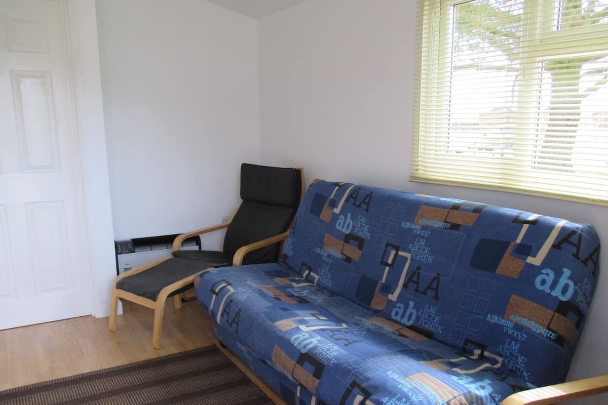 Una habitación con sofá, una silla, una mesita y una ventana con persianas.