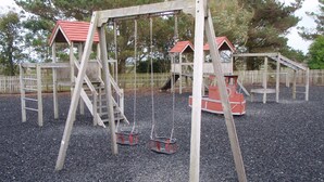Un parque infantil con columpios de madera y un módulo de juegos rojo.
