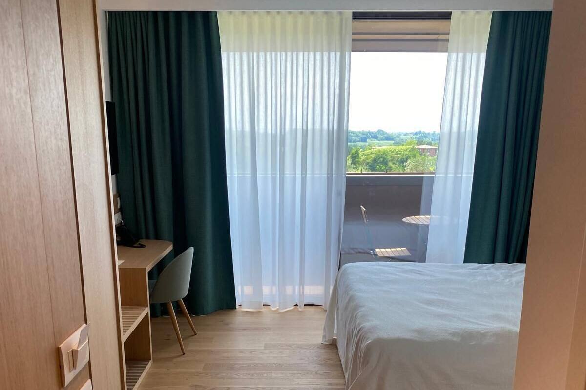 Ein Hotelzimmer mit Bett, Schreibtisch und Blick auf Grün durch das Fenster.