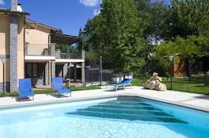 A swimming pool with blue lounge chairs, a stone statue, and a house with a balcony.