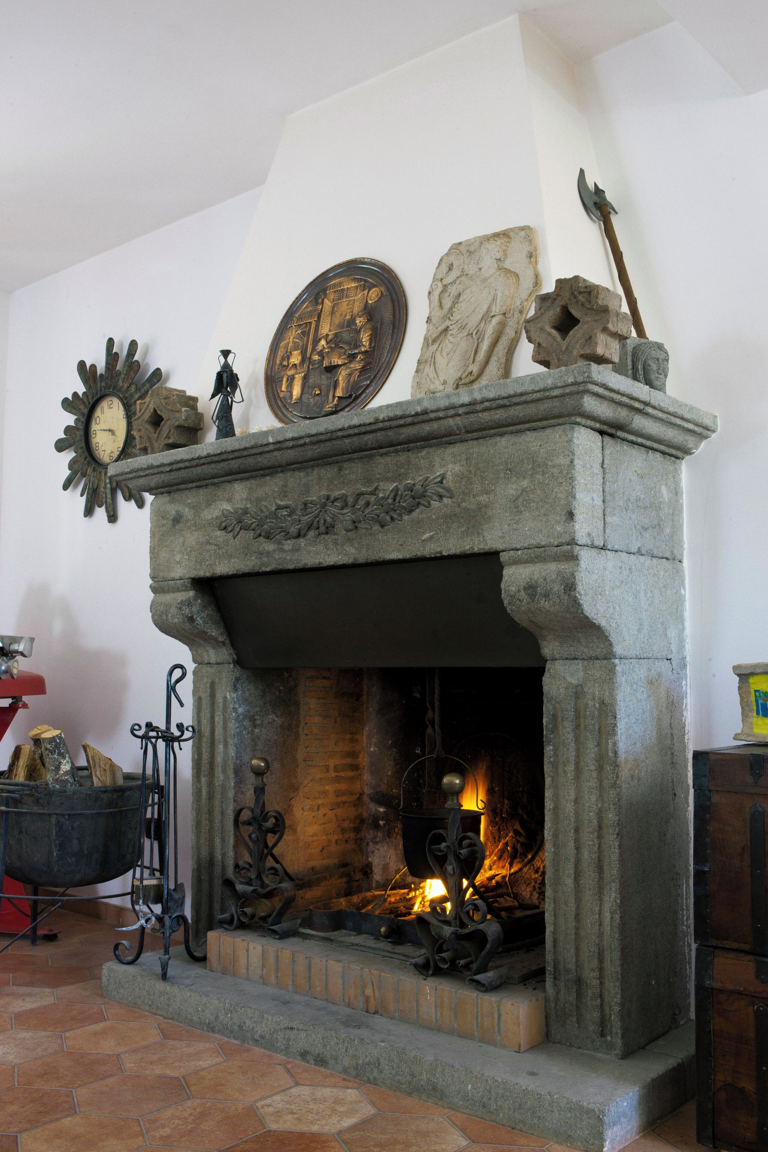 A stone fireplace with a fire, a clock, and decorative items on the mantel.