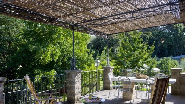 Un patio al aire libre con una pérgola, pilares de piedra, una mesa con sillas y una parrilla.
