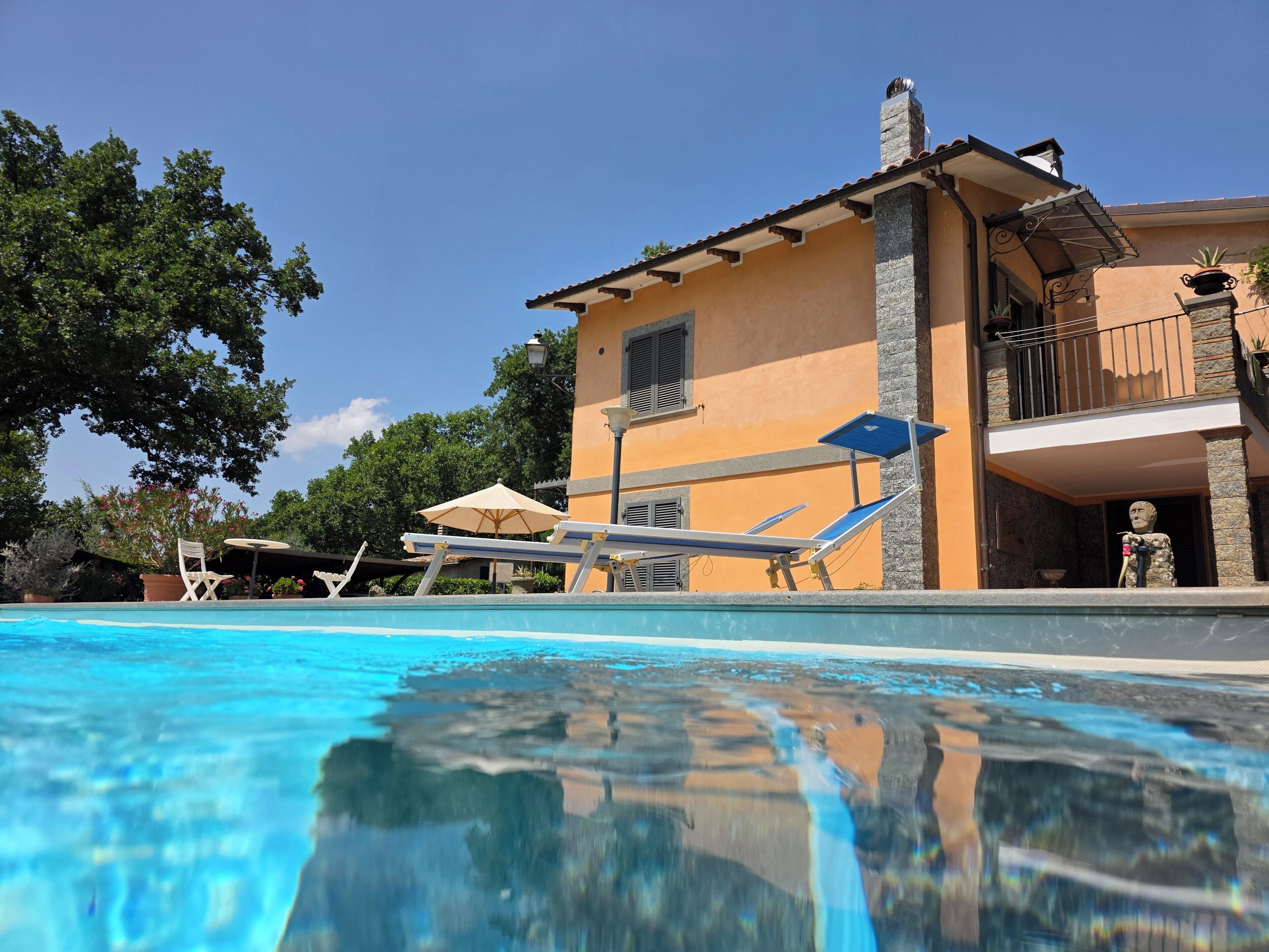 A swimming pool with lounge chairs and umbrellas, a building with a balcony, and a statue.