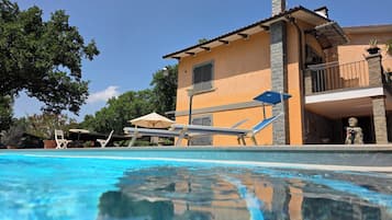 A swimming pool with lounge chairs and umbrellas, a building with a balcony, and a statue.