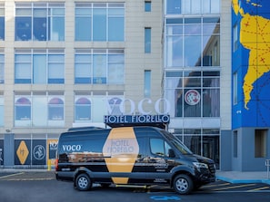 A black van with "Hotel Fiorrello" branding parked in front of a building with large windows and a blue map on the right side.