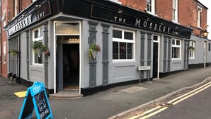 Un edificio en esquina con el letrero 'The Moseley Arms', fachada blanco y negro y cestas de flores colgantes.