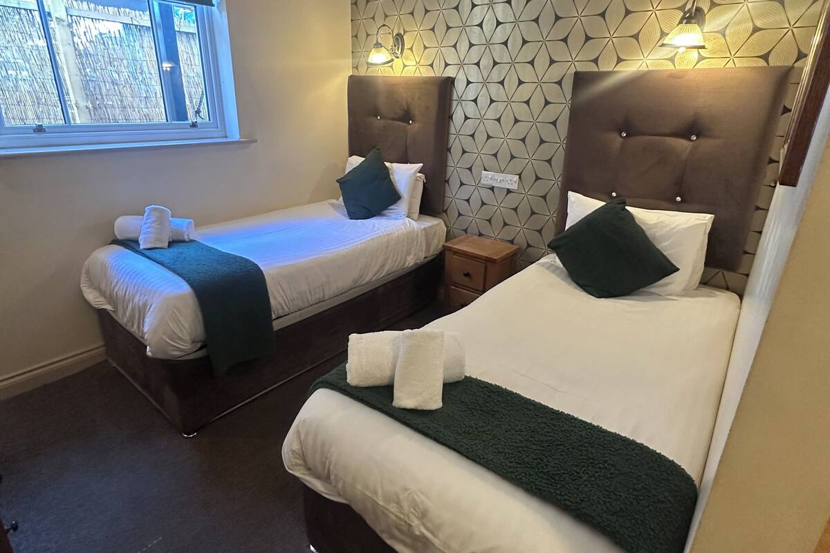 A hotel room with two beds, a window, a patterned wall, and a nightstand with a lamp.