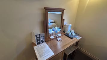 Habitación de hotel con escritorio de madera, espejo, televisor montado en la pared y mesita de noche con artículos de aseo.