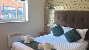 Una habitación de hotel con cama, ventana, calentador de pared y un diseño decorativo en la pared.