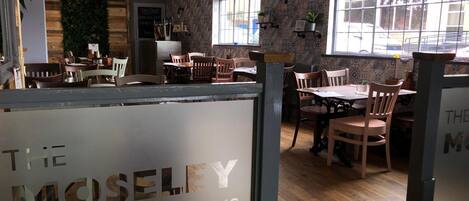 A restaurant interior with wooden furniture, a green wall, and patterned wallpaper.