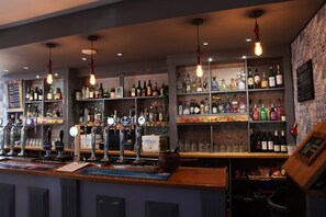 A bar with multiple shelves of liquor bottles, a variety of taps, and hanging light fixtures. - The Moseley Arms (Birmingham)