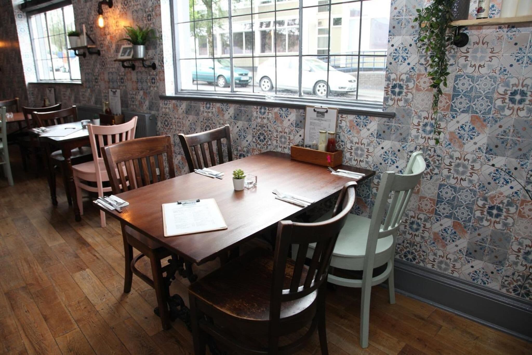 A restaurant interior with a wooden table, chairs, and patterned wallpaper.