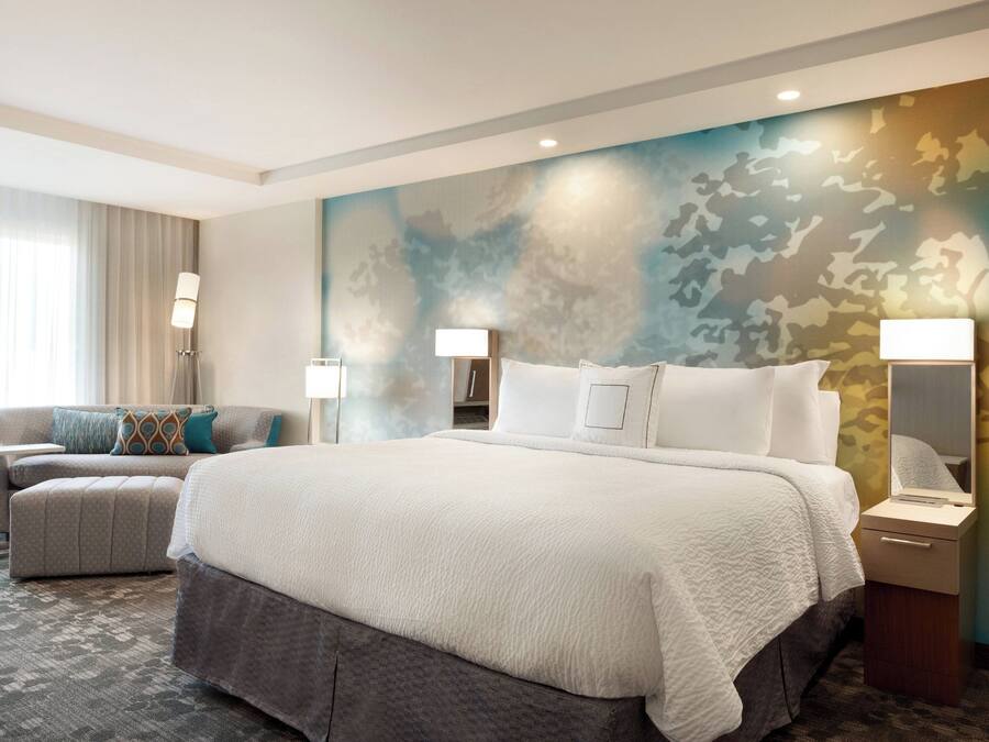 Una habitación de hotel con una cama grande, un sofá, una mesita y una lámpara.