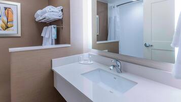 A modern bathroom with a white sink, a large mirror, and a shower area.