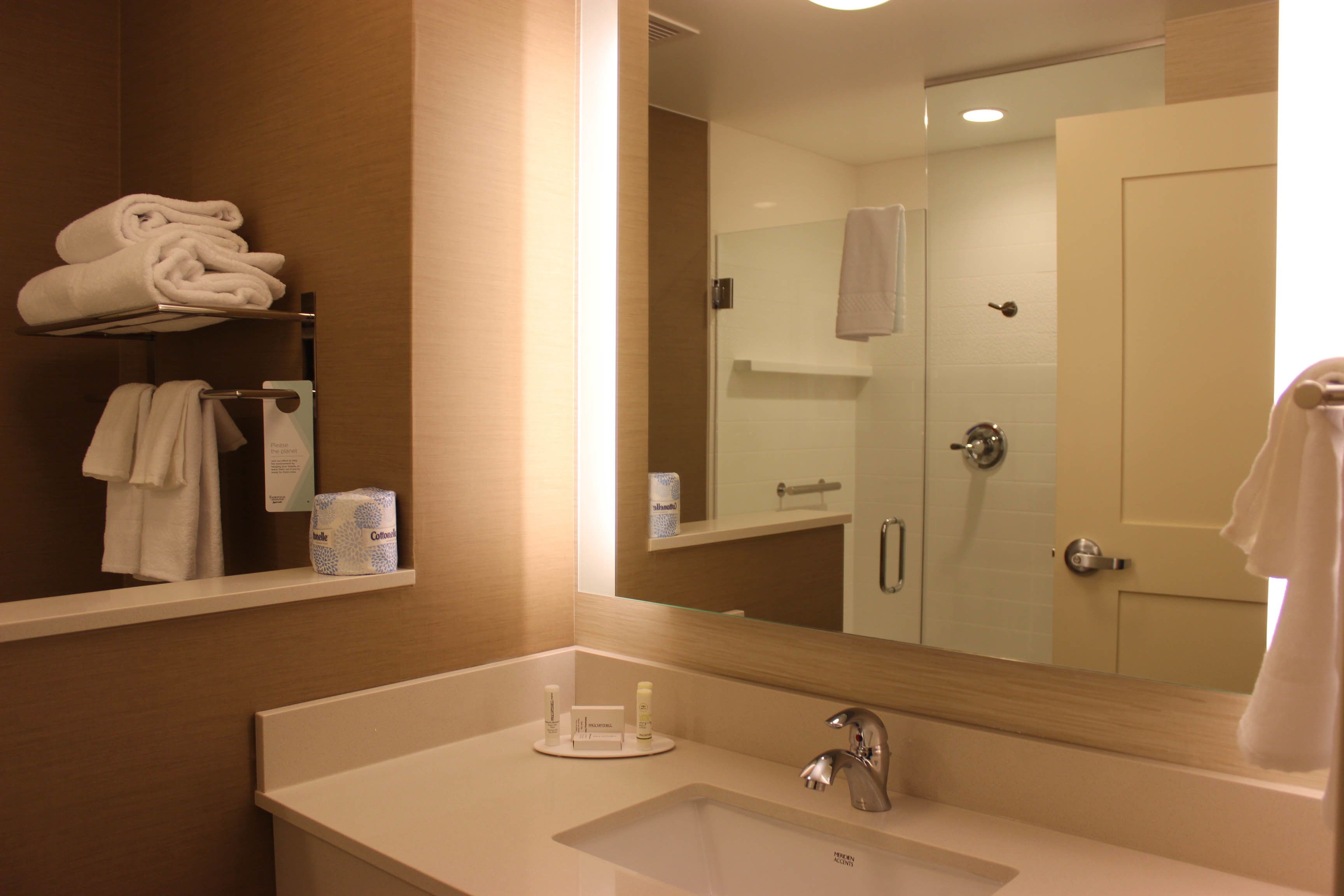 A hotel bathroom with a sink, mirror, towel rack, and a glass shower door.